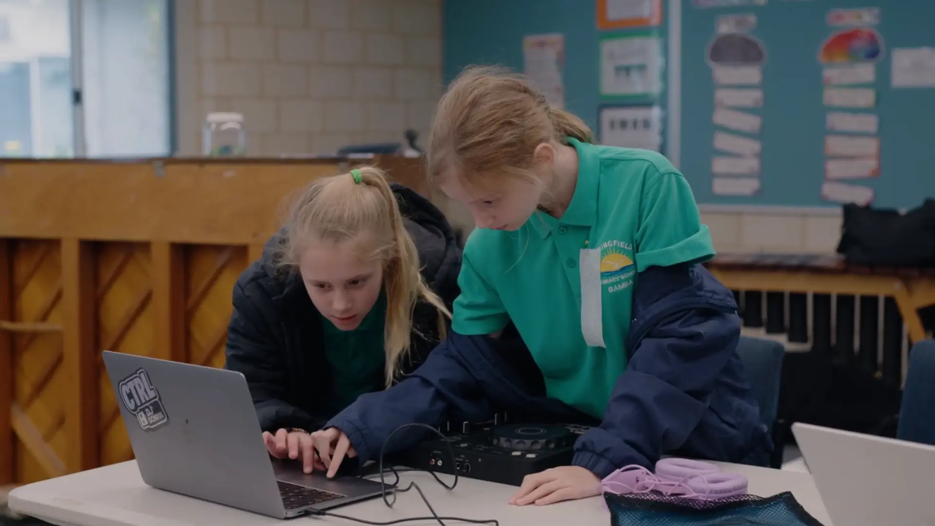 Two kids learning to DJ together on a laptop and controller